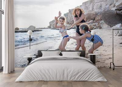 Happy young mother and her little daughters on the seashore in bathing suits. Wall mural