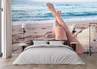 Legs of a woman relaxing on the beach by the sea. Wall mural