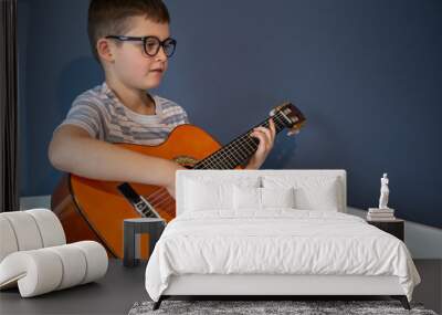 Little boy plays the classical guitar at home, on the bed. Wall mural