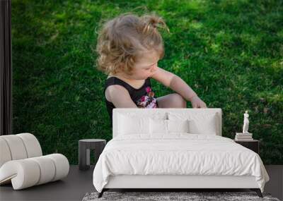 Little cute girl in summer sitting on the grass in the garden. Wall mural