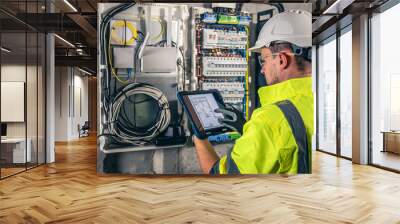 Man, an electrical technician working in a switchboard with fuses, uses a tablet. Wall mural