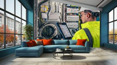 man, an electrical technician working in a switchboard with fuses, uses a tablet. Wall mural