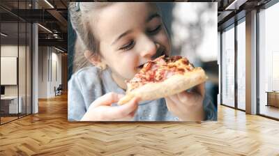 Portrait of a little girl with an appetizing piece of pizza. Wall mural