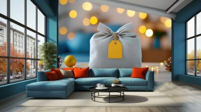 A Christmas present wrapped in a plain muslin bag, A beautifully wrapped gift with a yellow tag sits on a table, surrounded by festive decorations and warm bokeh lights, perfect for holidays. Wall mural