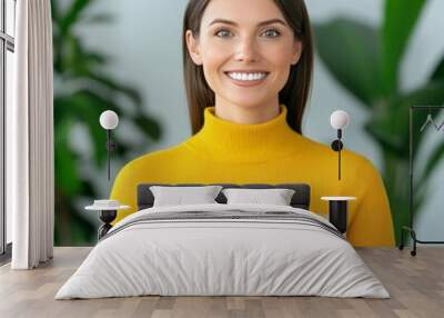 A smiling woman holding two cardboard boxes in front of a white wall with green plants behind her. Wall mural