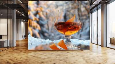 Glass of amber liquid with orange peel garnishes in front of a snowy background. Wall mural