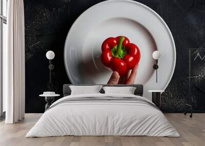 Hand holding red bell pepper over white plate on black background. Wall mural