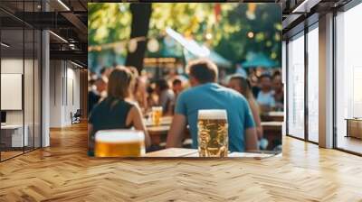 Two glasses of beer on a wooden table in a sunny outdoor setting with people blurred in the background. Wall mural