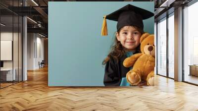 Faceless child in a graduation cap and gown holding a stuffed animal on a minimal light blue background Wall mural