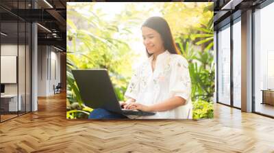 Happy Asian woman shopping online or working on laptop computer in garden at home. Buying or ordering on internet. Wall mural