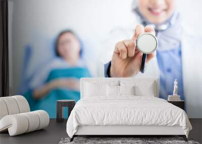 Muslim doctor showing stethoscope with blurred senior patient woman smiling on background. Hands focus Wall mural