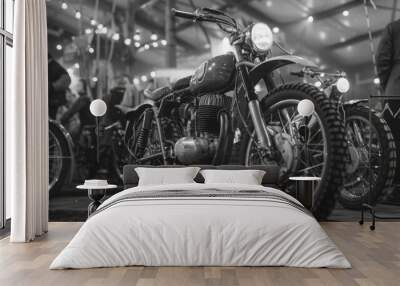 A black and white photo of a motorcycle with a man standing behind it Wall mural