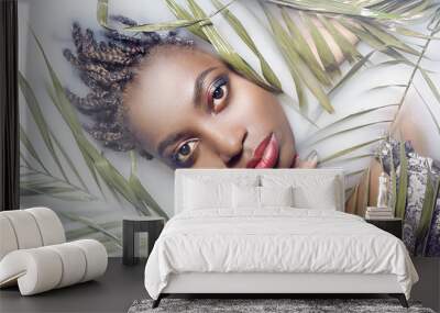 Girl African woman with bright makeup and clean the skin lies in the milk among the leaves so green Wall mural