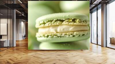 A close-up of a bite taken out of a green pistachio macaron, showing its creamy filling, with more macarons blurred in the background. Wall mural