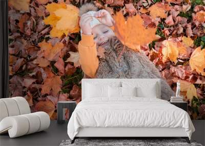 Portrait of a girl in a hat and vest lying in autumn leaves. Autumn. Emotions Wall mural