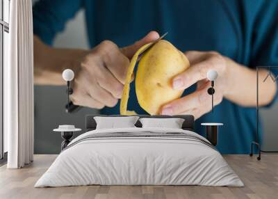 detail of hands of woman with blue sweater peeling fresh yellow potato with kitchen knife, horizontal
 Wall mural