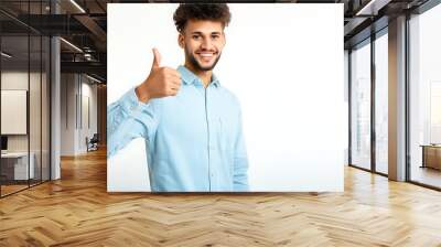 Young man displaying an upward thumb gesture on a white background, symbolizing success and praise. Wall mural