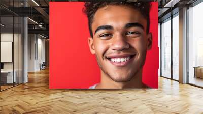 A close-up image capturing a smiling young man with curly hair, set against a bright and vibrant red background. Wall mural