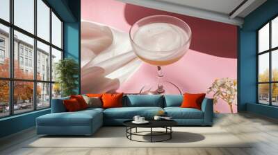 A sophisticated glass of cocktail sits next to delicate flowers, set against a pastel pink background with soft, ambient light. Wall mural