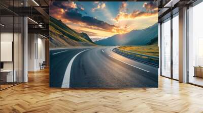 Breathtaking view of a winding road leading through mountainous terrain during a vibrant sunset Wall mural