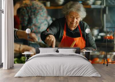 A smiling older woman cooks with a group of people in a kitchen.  They are preparing a meal together.  This is a stock photo of cooking class. Wall mural