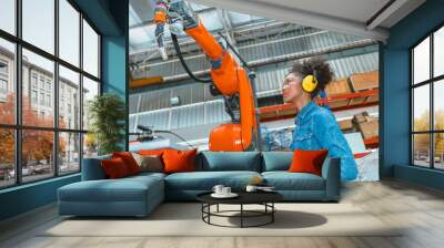 Engineer smart woman worker working programing robotic welding machine. Black teen girl work in advance modern factory. Wall mural