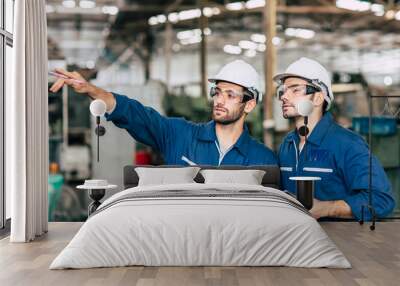 Two engineer worker working together with safety uniform and white helmet to work in industry checking production line. Wall mural