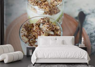 Dessert granola, greek yogurt, kiwi and banana in two glass cups with spoons on a wooden round board, gray concrete, close-up vertical frame format. Fitness, figure, body and healthy food Wall mural