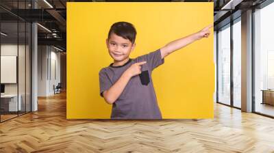 Adorable little Asian boy in casual t-shirt pointing finger to the empty space aside, showing or presenting your ads  Wall mural