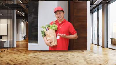 Asian delivery man carrying package box of fresh vegetable from grocery store in front of customer door outdoor.  Wall mural