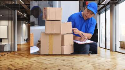 Courier in blue uniform with cap checking parcels and writing notes before send to customer Wall mural