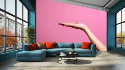 Female hand presenting and holding empty space for product placement or ads over pink background Wall mural