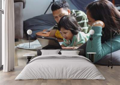 Happy Asian Family And Little Daughter Are Lying On Floor At Home Watching Digital Tablet Together
 Wall mural