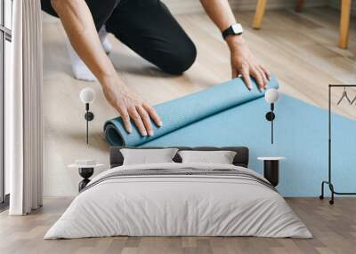 Man standing on knees and rolling exercise mat after yoga training at home Wall mural