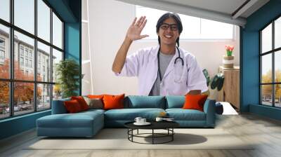 Portrait Of Doctor Man Wear White Coat And Stethoscope Greeting Wtih Waving Hand While Video Call With Patient Wall mural