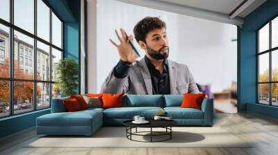 A confident businessman uses hand gestures to discuss growth strategies during a business meeting in a modern office, standing by a glass wall. Wall mural