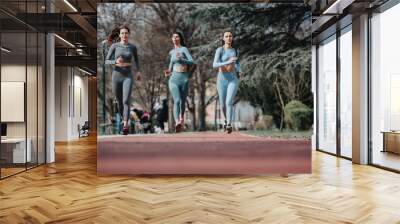 A dynamic photo of three female friends jogging together in a park, wearing sporty outfits and embodying a healthy lifestyle. Wall mural