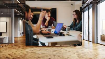 A group of focused colleagues engage in a lively discussion about work in a well-lit, contemporary office environment. Wall mural