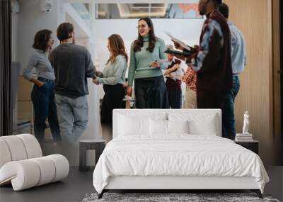 A group of multiracial colleagues engaging in a casual conversation in a brightly lit modern office space, exemplifying teamwork and networking. Wall mural