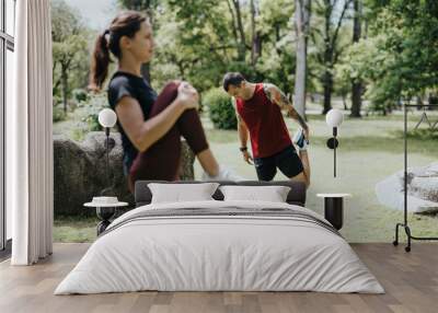 A man and a woman engage in stretching exercises in a lush green park, demonstrating healthy lifestyle and physical activity outdoors. Wall mural