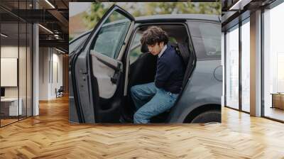 A teenage boy steps out of a car, ready for his school day. He wears casual attire and carries a backpack, conveying a morning routine and family care. Wall mural