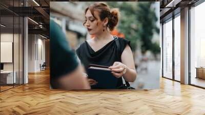 A young business entrepreneur engaged in an outdoor meeting on a busy city street, holding documents and emphasizing professional collaboration and communication. Wall mural