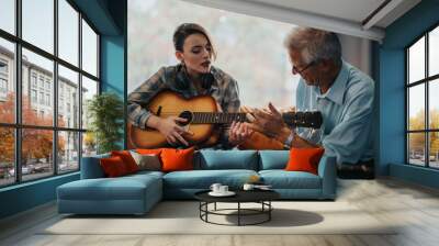 An elderly professor guides a young student in playing guitar during a music class. Together they explore musical techniques and creativity, fostering a learning environment. Wall mural