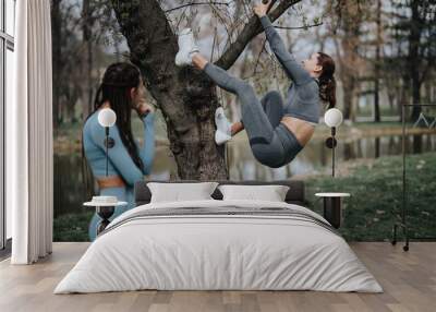 Athletic women engaged in sports activities on a tree in a scenic park setting, promoting health and fitness. Wall mural