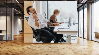 Business employee having phone call while working on the lap top at modern office setting. Wall mural