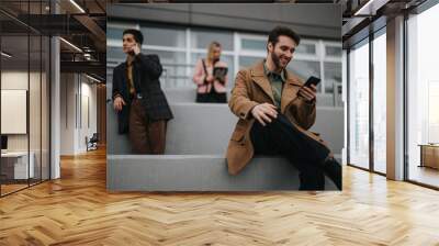 Cheerful male businessperson engaged on phone with team members nearby, modern corporate life depicted. Wall mural