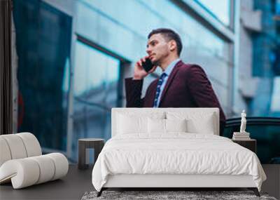 Entrepreneur(Businessman) standing in an urban area and wearing a suit and tie next to his limo while talking on the phone. Wall mural