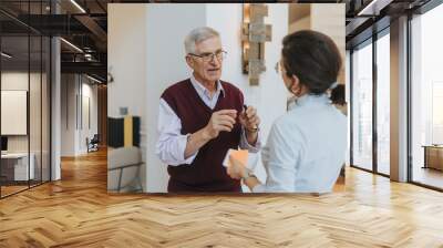 Experienced senior businessman in a conversation with a young female coworker. He gestures while holding a pen, in a bright modern office setting, signifying mentorship and collaboration. Wall mural