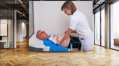 Female(doctor) nurse performs EKG test on an older man. Wall mural