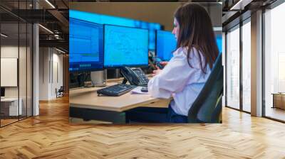 Female security guard sitting and monitoring modern CCTV cameras in a surveillance room. Wall mural